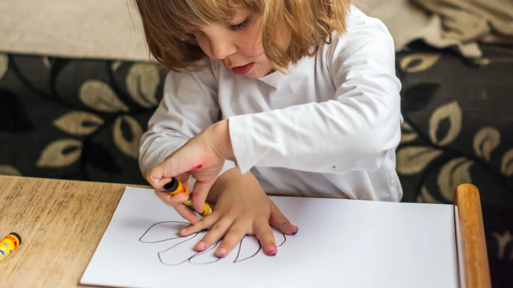 Coordination bilatérale enfant : un enfant trace le contour d’une main sur du papier, une main stabilisant pendant que l’autre dessine.