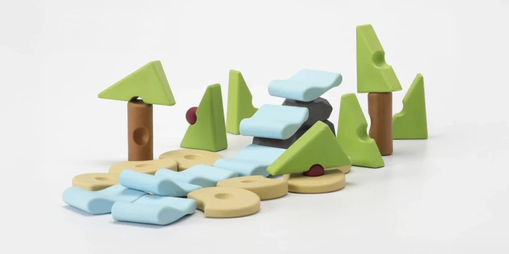 Jeu de construction libre en bois représentant une forêt avec un ruisseau, des arbres et des rochers sur fond blanc.